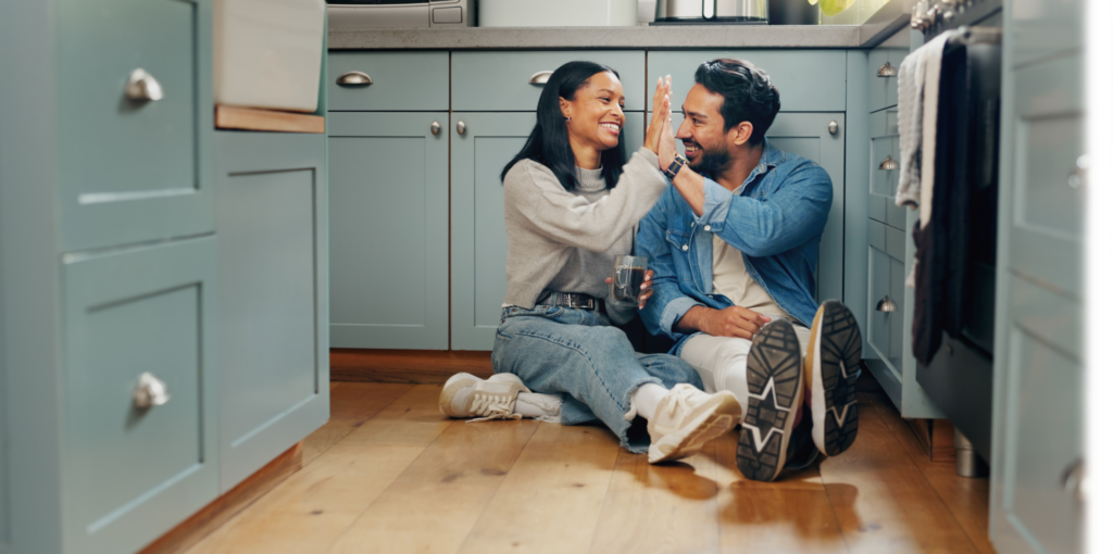 A couple high fiving sitting on their kitchen floor