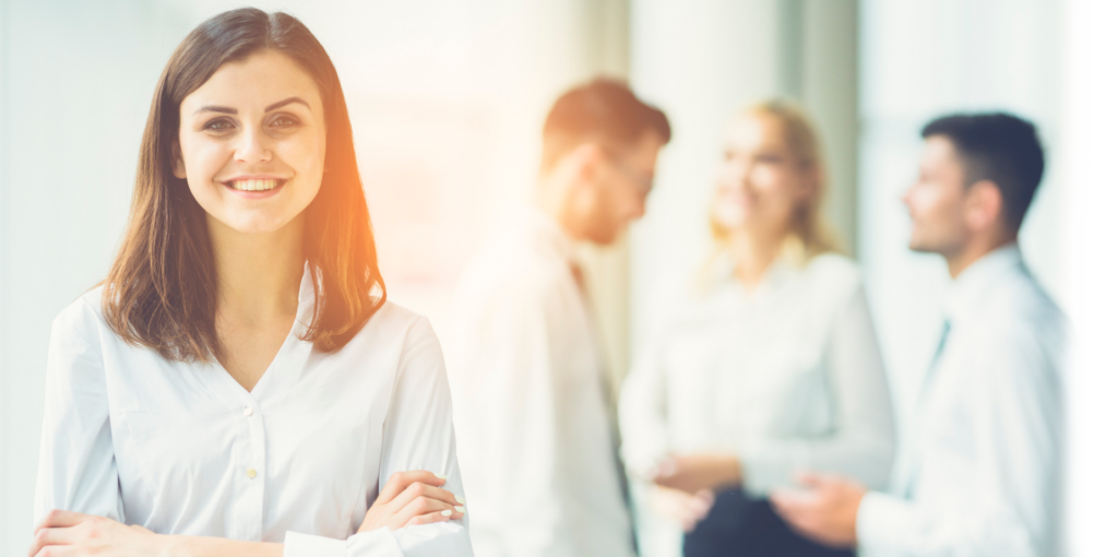 Smiling business woman with her arms crossed and colleagues in the back