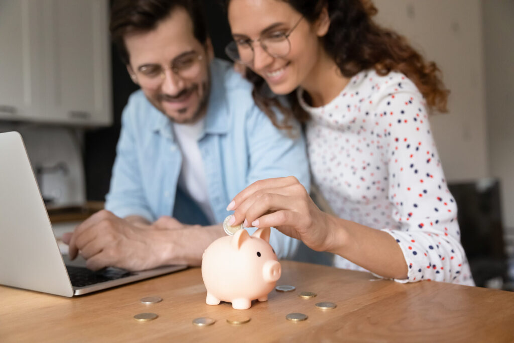 Happy millennial family couple putting coins in piggybank