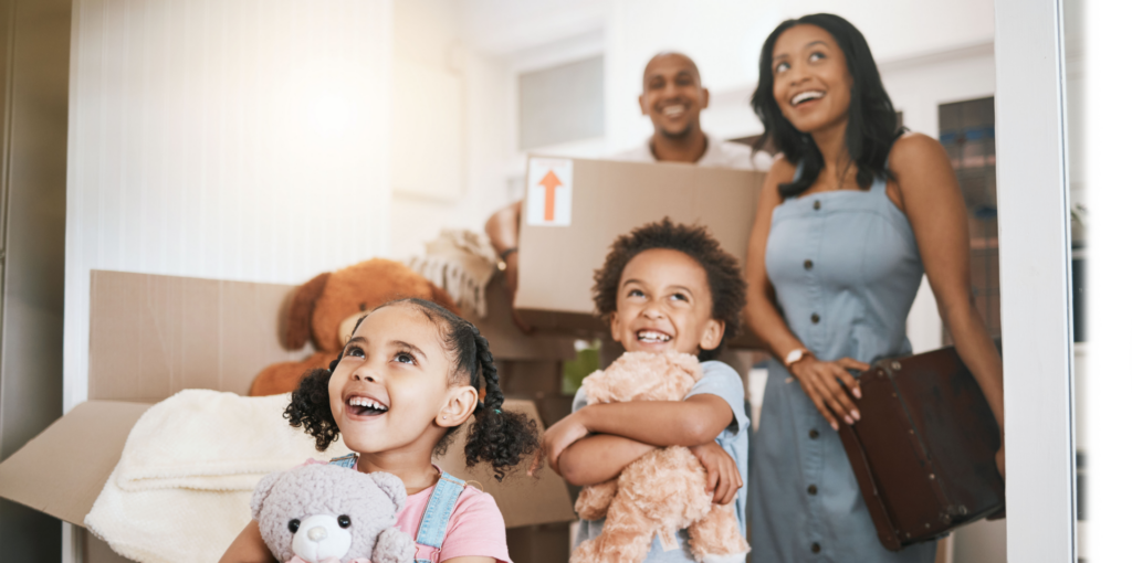 family smiling walking into new home with moving boxes.